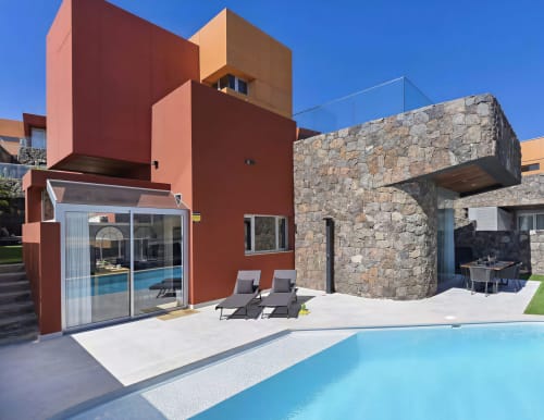 Modern red villa with stone accent at Home Stay Gran Canaria featuring private pool, loungers, and mountain views in Las