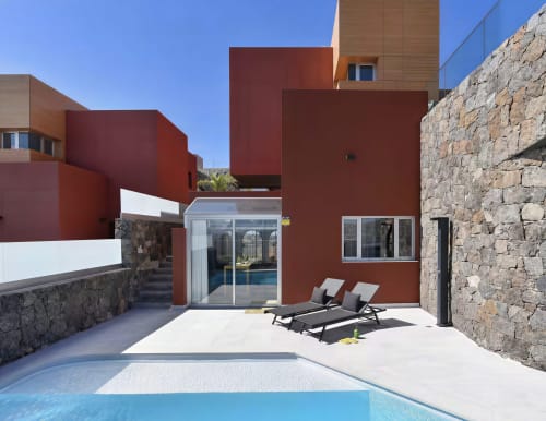 Modern red villa with private pool, lounge chairs, and stone walls at Home Stay Gran Canaria, Las Palmas