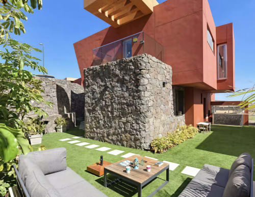 Modern villa with red architecture, stone courtyard tower, manicured lawn, outdoor furniture, and garden views in Las Palmas