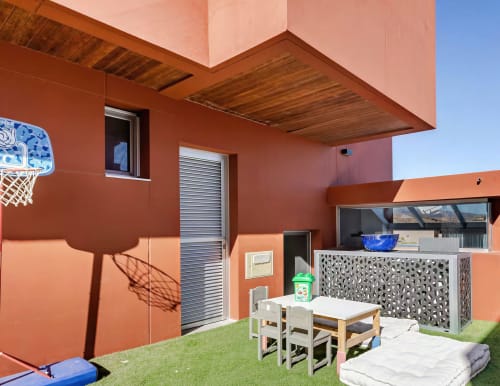 Modern villa patio at Home Stay Gran Canaria with orange walls, outdoor dining table, basketball hoop, and artificial grass