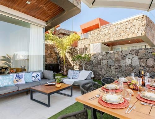 Modern outdoor terrace at Home Stay Gran Canaria villa with dining table, lounge seating, stone walls, and mountain views in