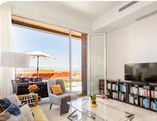 Modern villa living room with pool view terrace, comfortable seating, bookshelf, and ocean landscape at Home Stay Gran