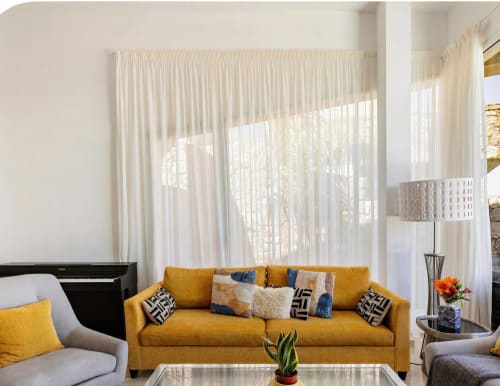 Bright modern villa living room with mustard yellow sofa, floor-to-ceiling sheer curtains, and pool views in Gran Canaria