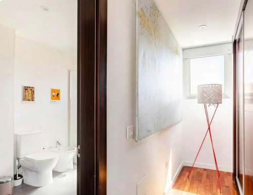 Modern bathroom hallway with white walls, wooden flooring, floor lamp with red tripod, and small framed artworks at Home Stay
