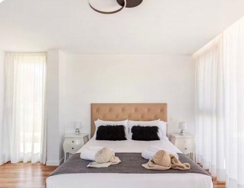 Bright modern bedroom with tan upholstered headboard, white bedding, black accent pillows, and beige throws at Home Stay Gran