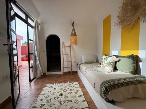 Chambre lumineuse à l'hôtel Eucalyptus Ethnic d'Essaouira avec lit, accents jaunes, porte-fenêtre et décor bohème