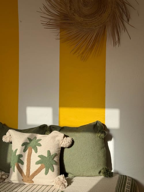Coussins décoratiefs aux broderies de palmiers sur lit dans la suite panoramique de l'hôtel Eucalyptus à Essaouira, mur jaune et