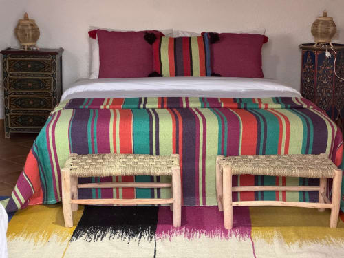 Lit à rayures colorées dans la suite de l'hôtel Eucalyptus à Essaouira, avec bancs tissés et décoration traditionnelle