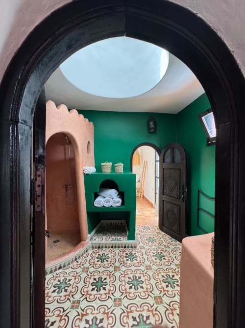 Salle de bains verte marocaine avec carrelage zellige, porte noire cintrée et rangements de serviettes à l'hôtel Eucalyptus, Essaouira