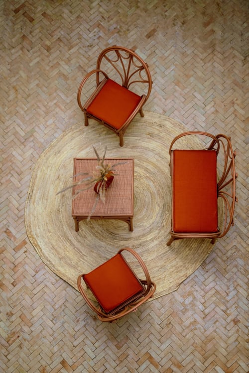Vue aérienne du patio du riad avec trois fauteuils en rotin à coussins rouges sur un tapis tissé circulaire au Riad Dabachi Tala'lou