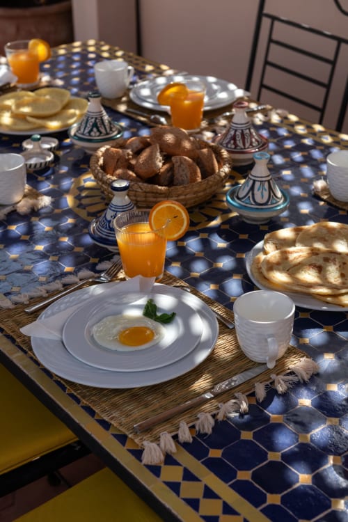Petit-déjeuner marocain au Riad Dabachi Tala'lou avec œuf frit, jus d'orange, pain et tajines sur motifs bleus