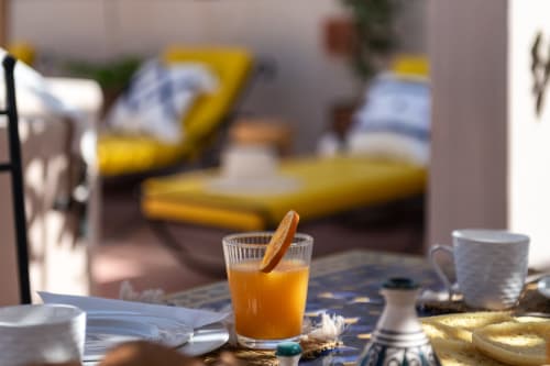 Jus d'orange et pâtisserie au petit-déjeuner du Riad Dabachi Tala'lou à Marrakech, sièges jaunes visibles dans la cour