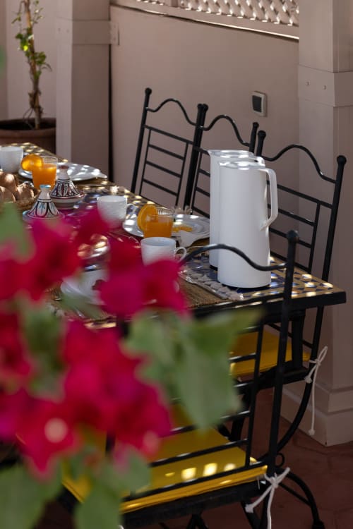 Élégante mise de table au Riad Dabachi Tala'lou de Marrakech avec fleurs roses, pichet blanc et chaises noires