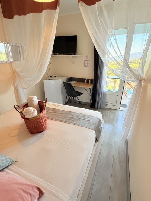 Chambre double lumineuse avec voilages, balcon vue mer, TV, bureau et panier de bienvenue à l'Hôtel le soleil couchant