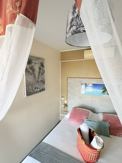 Chambre double aux influences tropicales à l'Hôtel le soleil couchant, vue mer, teintes roses, décor de palmiers et voilages délicats.