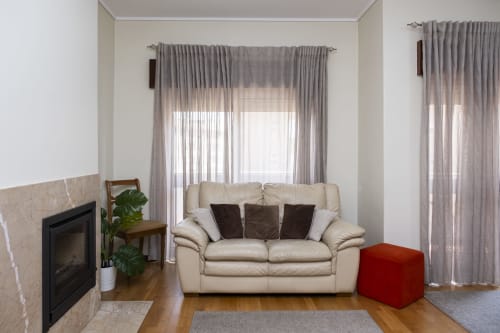 Moderna sala de estar no Apartamento RH Charming em Barcelos com sofá creme, lareira e cortinas cinzas com vista para a cidade