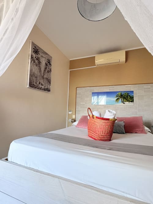 Chambre double lumineuse à l'Hôtel le soleil couchant avec vue sur mer, literie blanche, panier décoratif et œuvres d'art tropicales