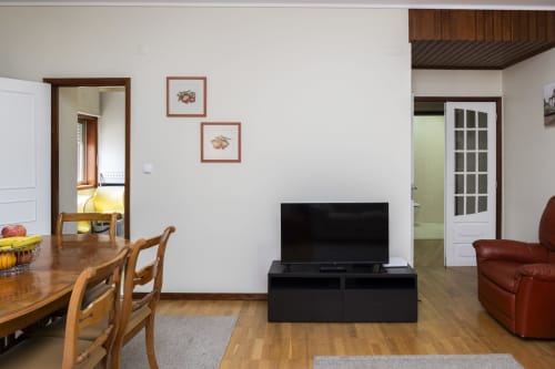 Sala de estar integrada no Apartamento Encantador RH, Barcelos com mesa de jantar, TV, sofá vermelho e piso em madeira