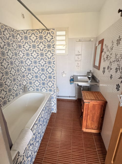 Salle de bain moderne avec carrelage de douche à motifs bleus, meuble-lavabo en bois et murs en lambris blanc à l'Hôtel le soleil couchant, St