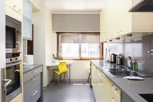 Cozinha moderna no Apartamento Encantador RH, Barcelos com armários creme, bancadas pretas e eletrodomésticos em aço inoxidável