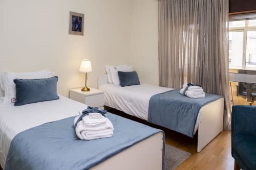 Camas gêmeas com detalhes azuis em um quarto brilhante com vista para a cidade em RH Charming Apartments, Barcelos, com design moderno