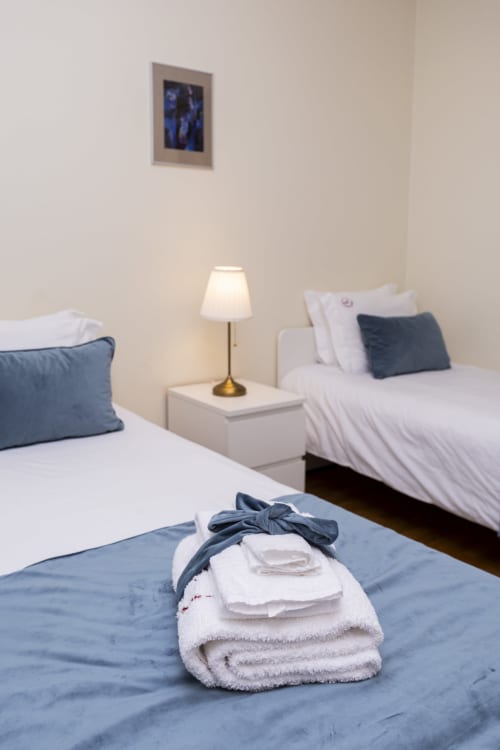 Quarto moderno no RH Charming Apartments em Barcelos com camas de solteiro, toalhas dobradas e luminária de cabeceira