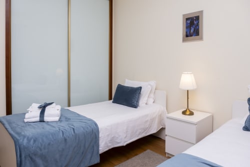 Quarto moderno no RH Charming Apartment em Barcelos com camas de solteiro, roupas de cama brancas, detalhes azuis e vista para a cidade