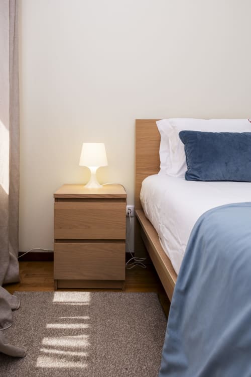 Quarto moderno no RH Charming Apartments Barcelos com criado de madeira, luminária acesa e cama perfeitamente arrumada com roupa de cama branca