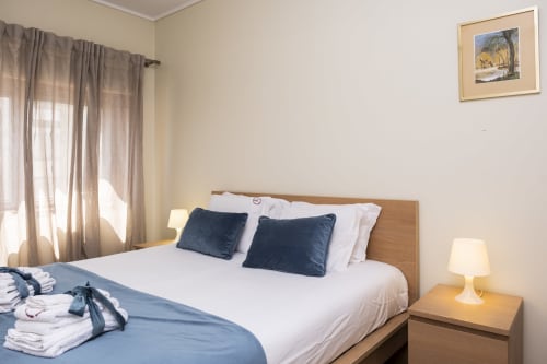 Quarto moderno no RH Charming Apartments Barcelos com cama de madeira, almofadas escuras, roupas de cama brancas e vista para a cidade