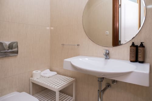 Banheiro moderno no RH Charming Apartments em Barcelos com pia branca, espelho redondo e azulejos bege