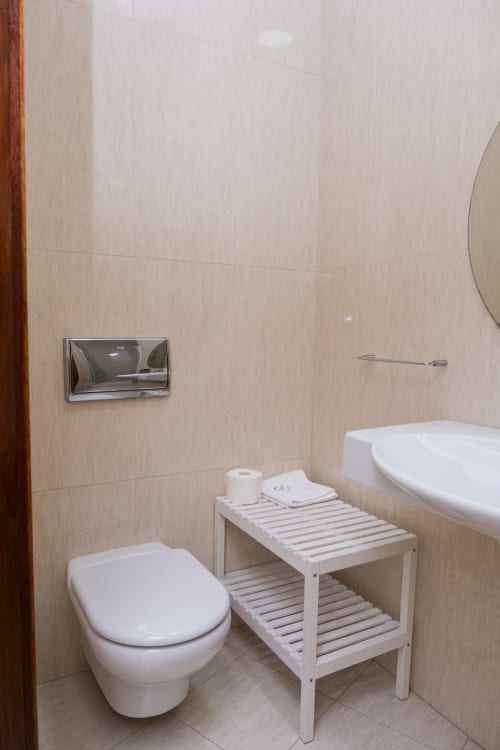 Banheiro moderno no RH Charming Apartments em Barcelos com vaso sanitário suspenso, prateleiras brancas e paredes em azulejos bege