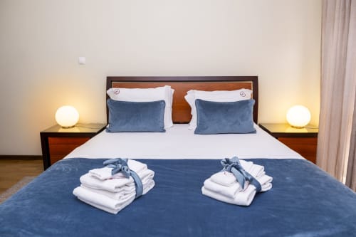 Quarto luxuoso no RH Charming Apartments em Barcelos com roupas de cama azul e branca, abajures duplos e toalhas enrolladas