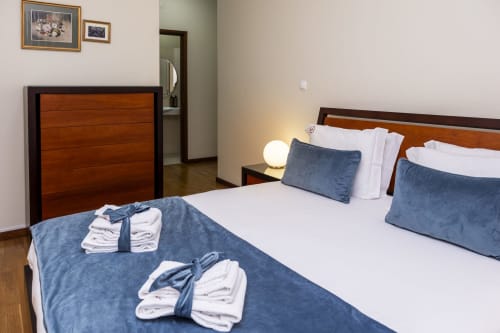 Quarto espaçoso no RH Charming Apartments em Barcelos com duas camas, almofadas azuis, roupas de cama brancas, móveis de madeira e vista da cidade