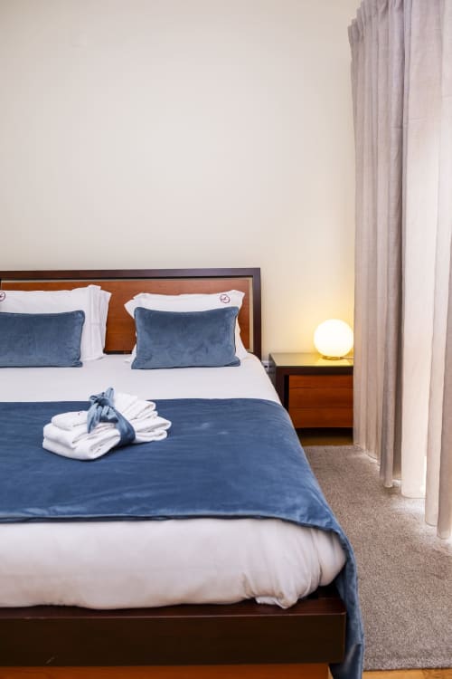 Quarto moderno no RH Charming Apartments em Barcelos com almofadas de veludo azul, roupas de cama brancas, cabeceira de madeira e aconchego