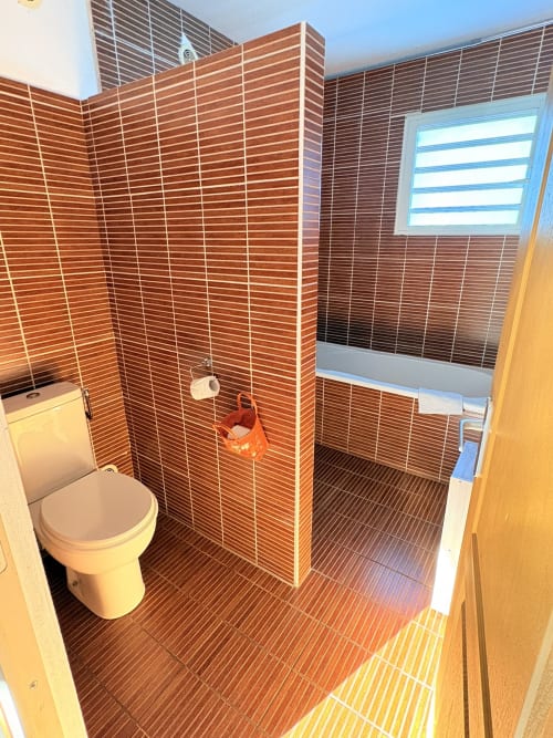 Salle de bains moderne aux carreaux rouges, toilettes blanches et douche à l'italienne à l'Hôtel le soleil couchant, St Pierre