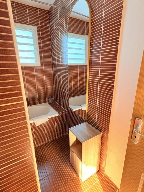 Salle de bains moderne avec murs en brique rouge, douche vitrée et meuble-lavabo en bois à l'Hôtel le soleil couchant, St Pierre
