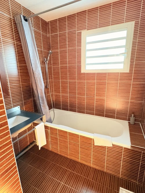 Salle de bain moderne avec carrelage en brique rouge, baignoire blanche et douche à l'Hôtel le soleil couchant, Saint-Pierre, La Réunion