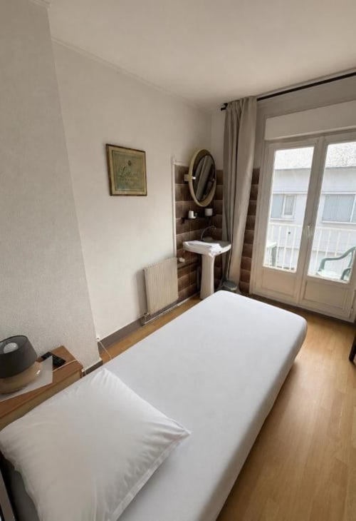 Chambre single avec lit blanc, lavabo sur colonne, carrelage mural marron et vue sur balcon à l'Hôtel bistrot de la poste
