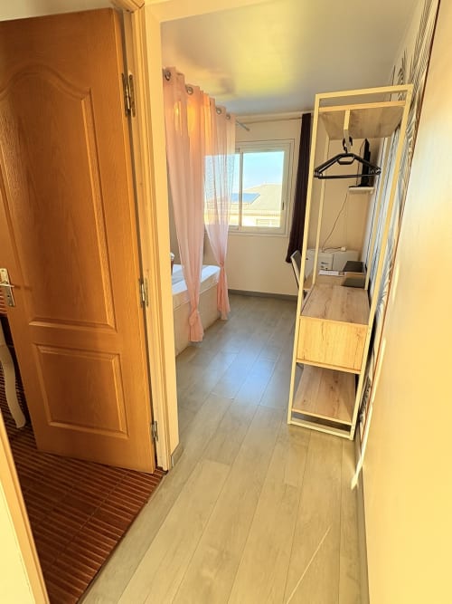 Entrée de la chambre C5 de l'Hôtel le Soleil Couchant avec porte en bois, couloir, miroir, armoire et fenêtre donnant sur le jardin