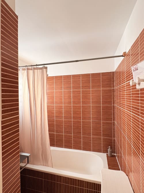 Salle de bains moderne avec carrelage en terre cuite, baignoire blanche et rideau de douche rose à l'Hôtel le soleil couchant, St Pierre
