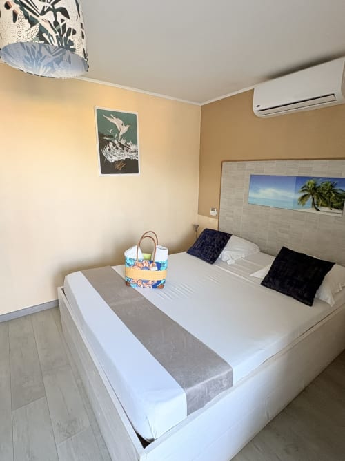 Chambre double Hôtel le soleil couchant avec lit blanc, oreillers noirs, décoration tropicale, climatisation et thème balnéaire
