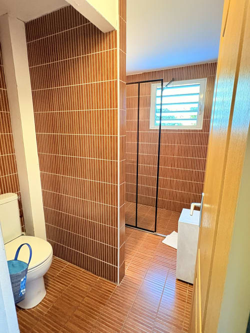 Salle de bain moderne avec carrelage linéaire marron, toilettes blanches, lavabo sur colonne et douche vitrée à l'Hôtel le soleil