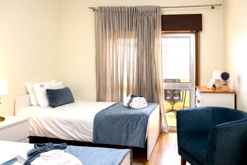 Quarto brilhante no RH Charming Apartments em Barcelos com cama branca, detalhes azul escuro e vista para a cidade pela porta da varanda