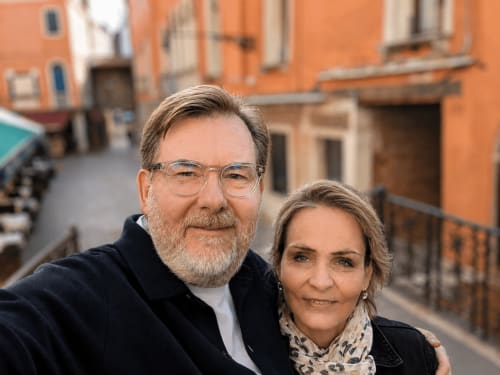 Deux personnes souriantes devant la Conciergerie Saint Martin, un hôtel parisien, avec des bâtiments orange en arrière-plan