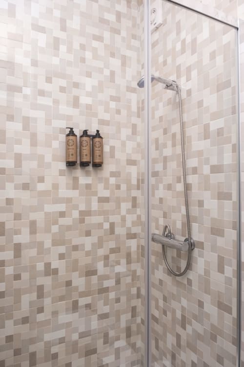 Chuveiro moderno com azulejos mosaico bege e branco, porta de vidro e três garrafas de amenidades no RH Charming Apartments