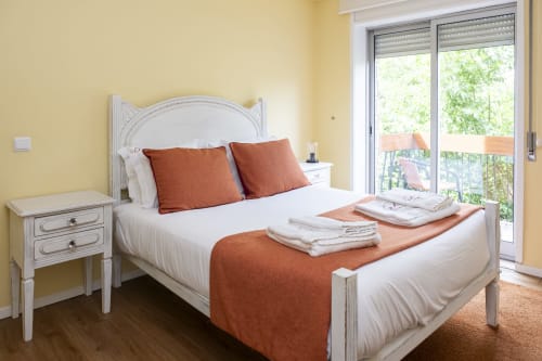 Quarto luminoso no RH Charming Apartments em Braga com cama branca, almofadas laranja e acesso à varanda