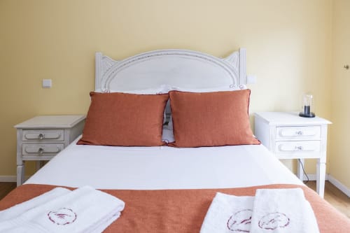 Quarto acolhedor no RH Charming Apartments em Braga com cabeceira branca, almofadas de terracota e mesas de cabeceira combinadas