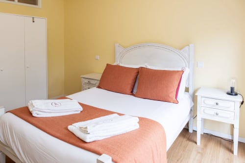 Quarto brilhante no RH Charming Apartments Braga com cama queen, almofadas laranja, criado branco e paredes amarelo quente