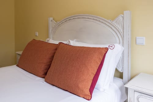Quarto elegante nos RH Charming Apartments em Braga com cabeceira branca ornamentada e almofadas cor ferrugem em roupa de cama branca