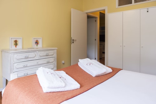 Quarto brilhante no RH Charming Apartments em Braga com cômoda branca, guarda-roupa, paredes amarelas e toalhas arrumadas